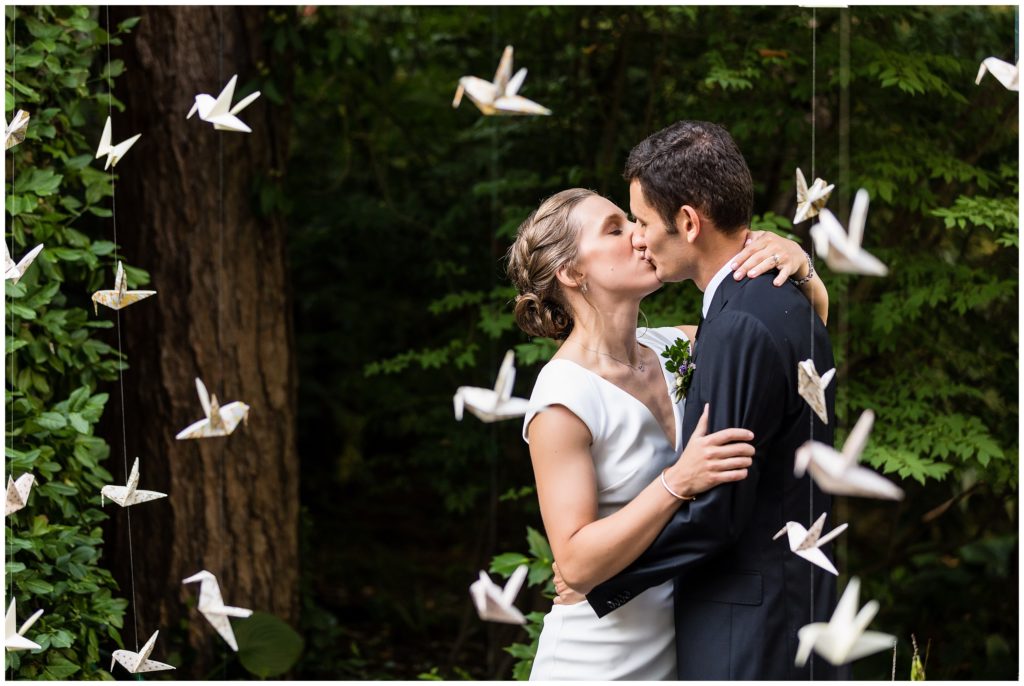 Bride and groom kissing in wall of hanging hand made paper cranes at outdoor Old Mill wedding