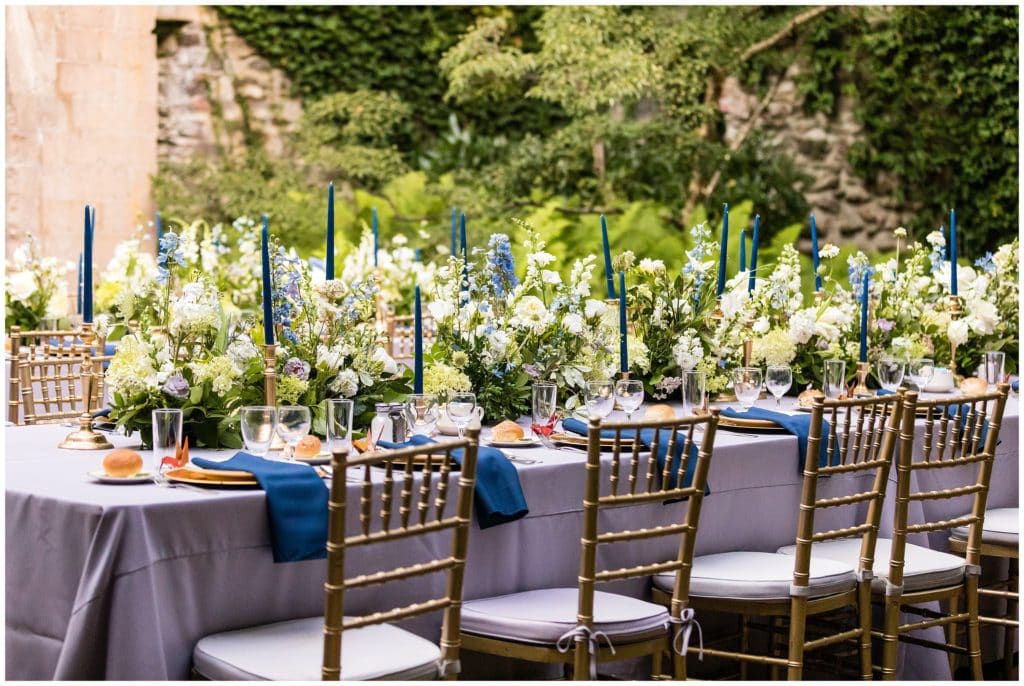 Intimate outdoor wedding reception table setup with purple and blue linens, blue candle and green, purple, and blue centerpiece florals at Old Mill