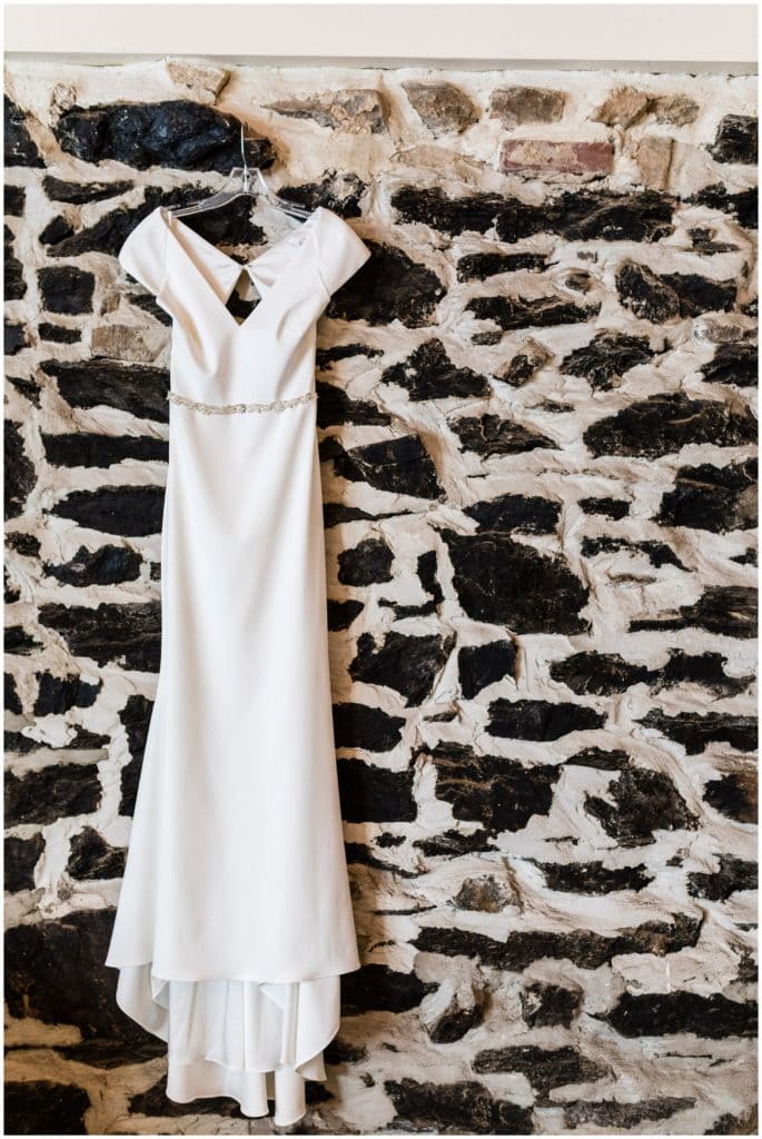 Simple wedding gown hanging on stone wall