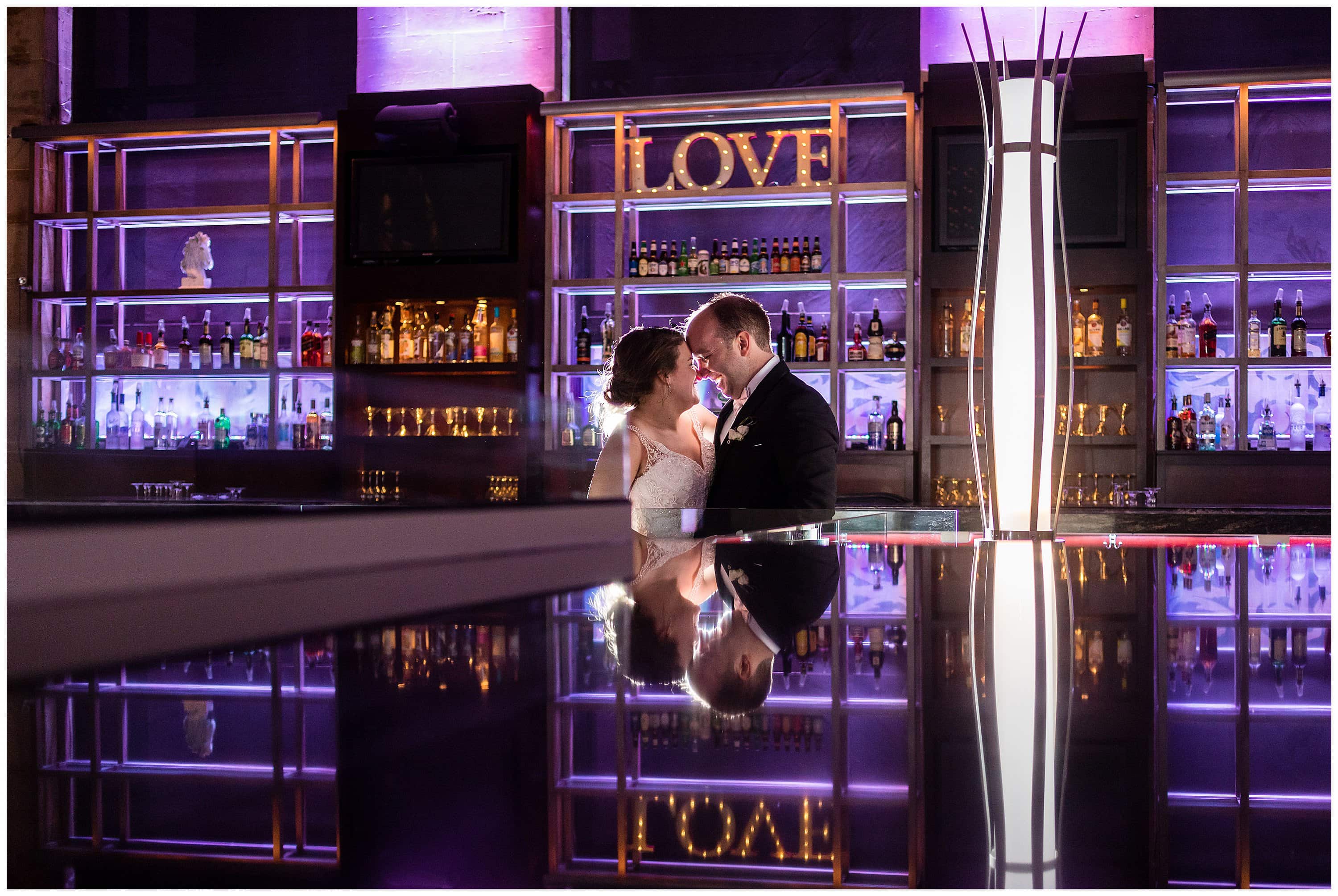 portrait of bride and groom behind the bar and reflecting off the bar at Union Trust in front of the Love sign - best Philadelphia wedding venues