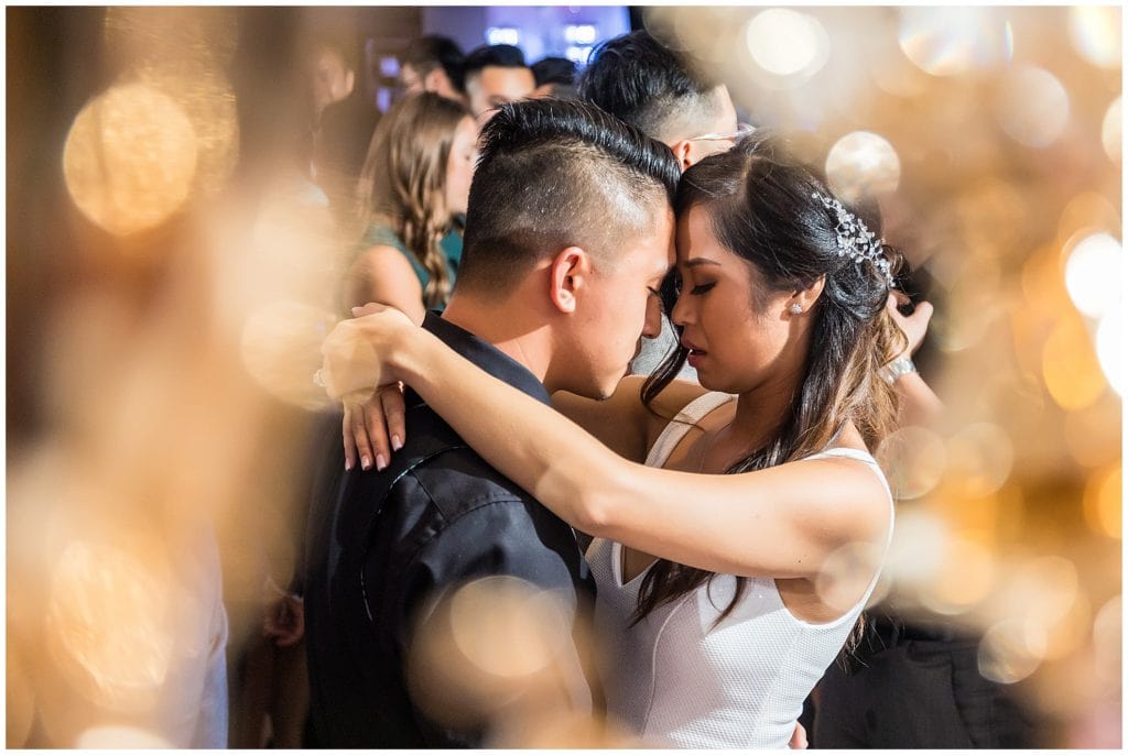 Bride and groom having a close moment on the dance floor shot through gold lights