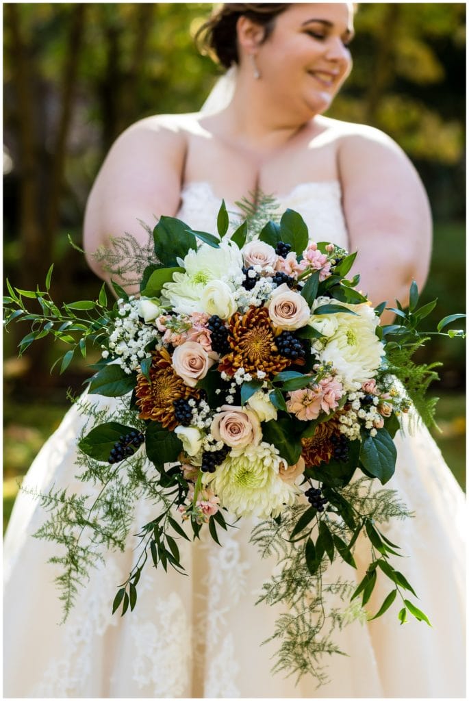 detail of bride showing off her autumn inspired wedding bouquet featuring greenery and berries