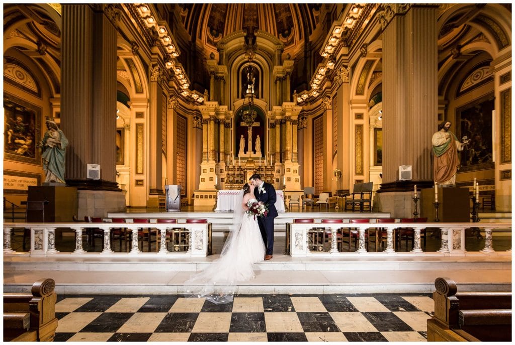 Traditional bride and groom kissing at St. Joe's Prep alter, Church of the Gesu wedding ceremony