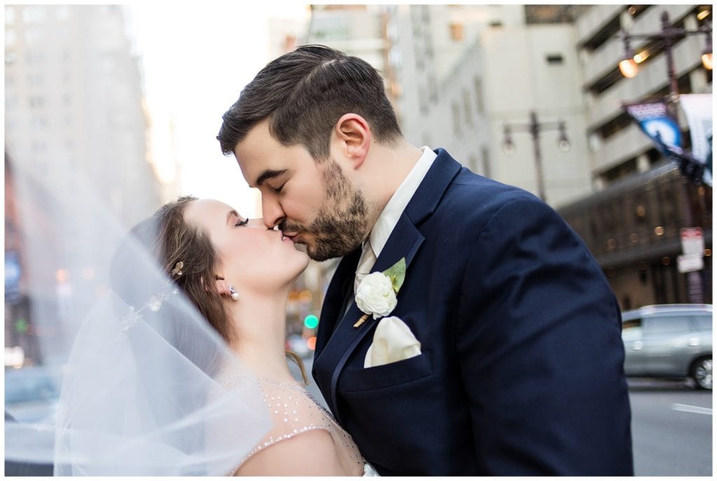 Bride and groom kiss with veil blowing in the wind in Philadelphia wedding