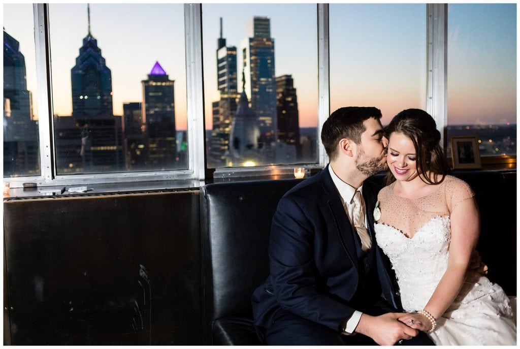 Groom kissing bride on the cheek with Philadelphia skyline background