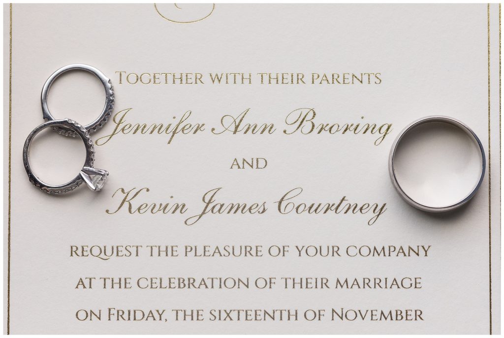 White and gold wedding invitation with wedding bands and engagement ring