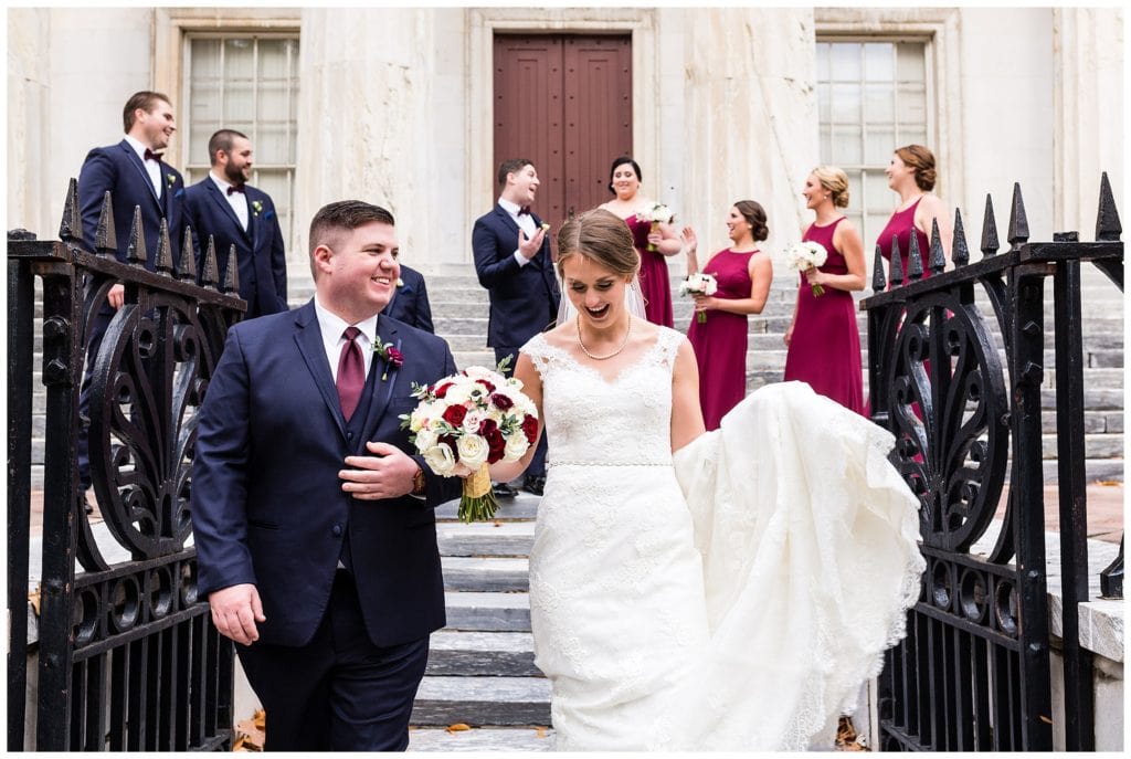 Bride and groom walking through gate with wedding party on steps at Second National Bank in Philadelphia