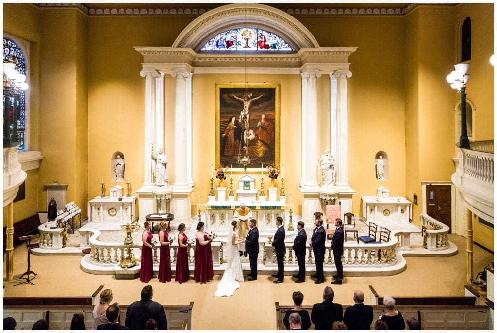 Bride and groom stand with wedding party at Old St Joe's Church alter, Old St Joseph's Church wedding in Philadelphia