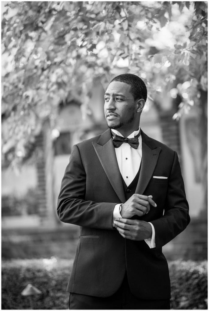 Traditional black and white groom portrait outside adjusting cufflinks