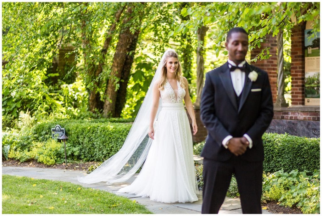 Groom waiting for bride walking toward him during first look at Aldie Mansion wedding