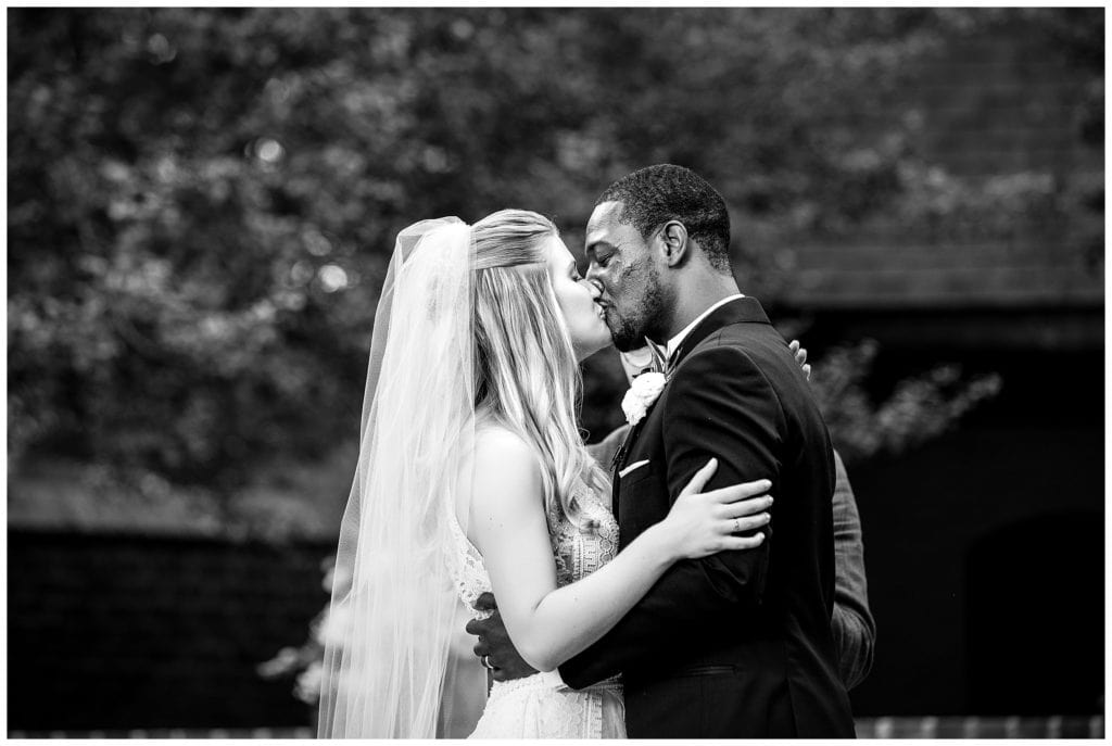 Traditional black and white wedding portrait with bride and groom sharing first kiss at Aldie Mansion outdoor wedding ceremony