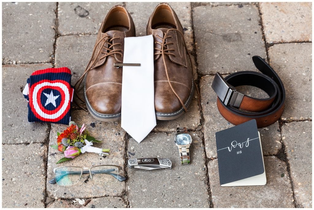 Groom details with shoes, Captain America socks, vow book, glasses, custom pocket knife, watch, and boutonniere