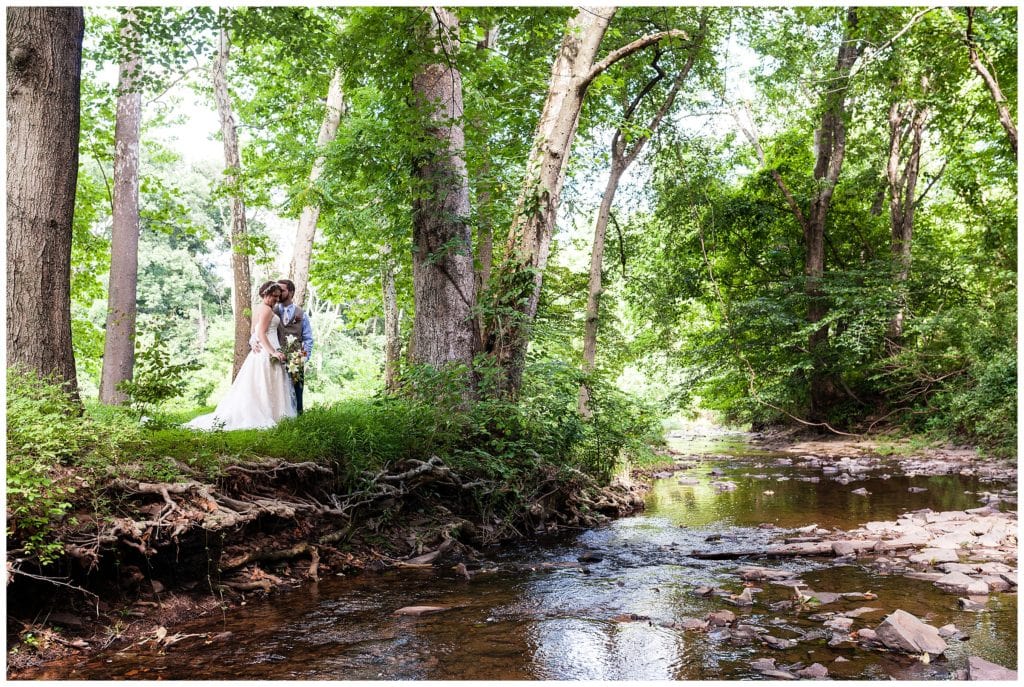 Romantic bride and groom kissing portrait next to creek at Barn on Bridge wedding