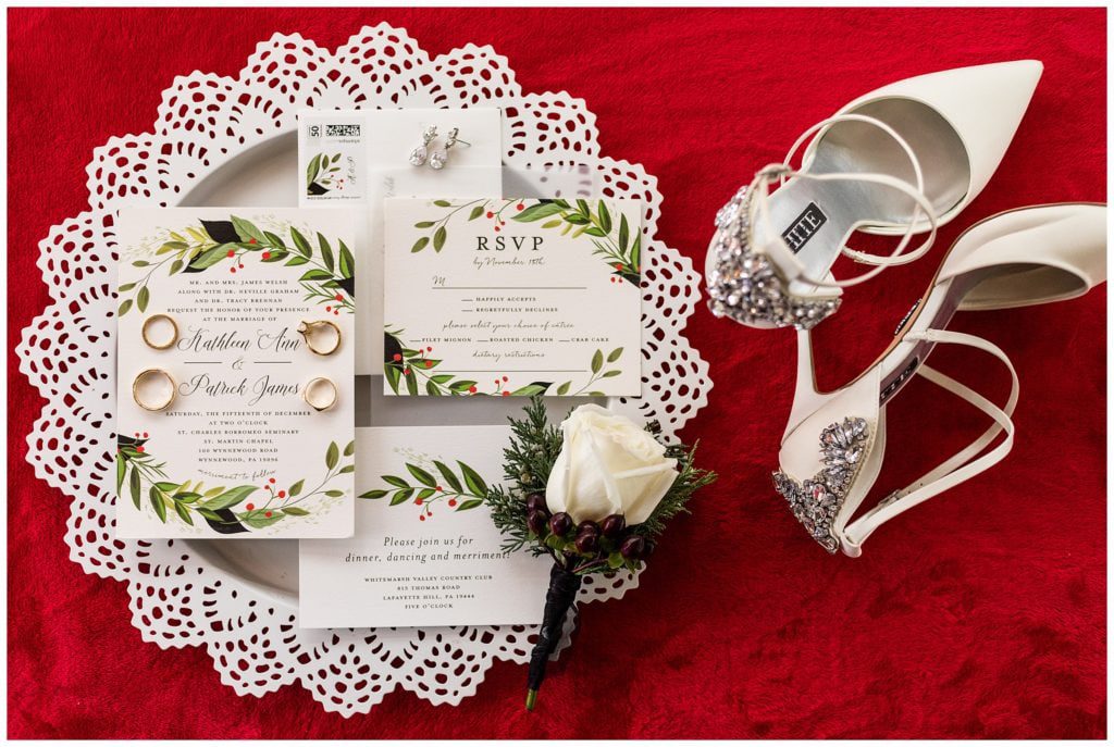 Red and green Christmas themed wedding invitation suite with white wedding heels, pine and rose boutonniere, and gold wedding rings