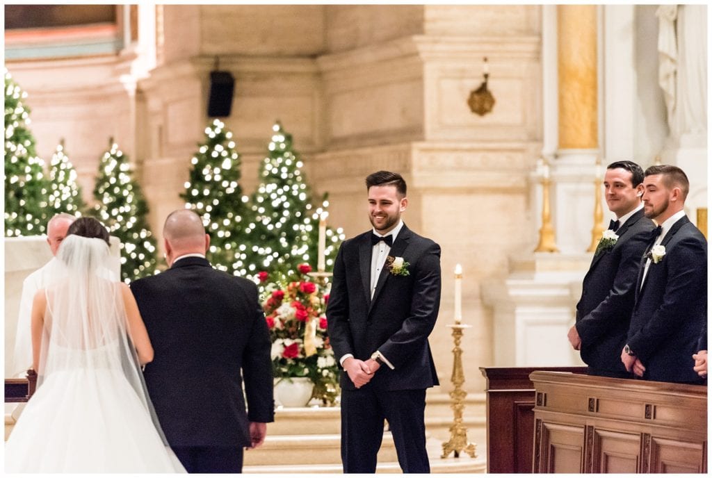 Groom smiling at bride walking down aisle in St. Charles Boromeo Church Christmas wedding ceremony