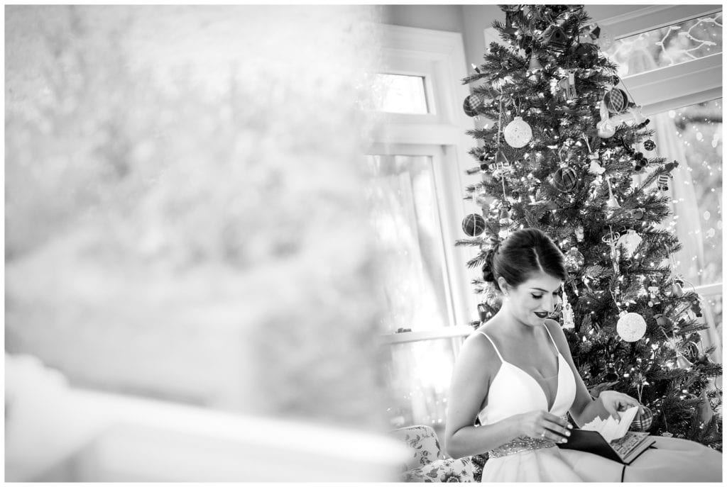 Black and white bridal portrait of bride reading letter from groom in front of Christmas tree