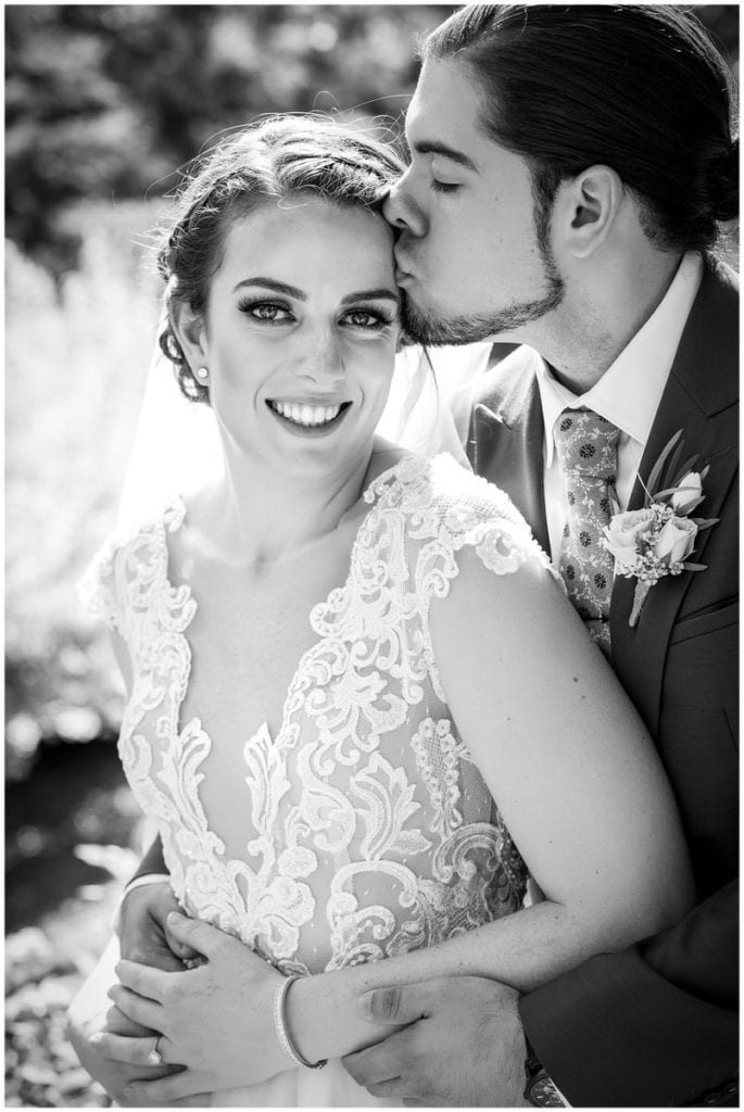 Black and white wedding portrait of groom kissing bride on forehead