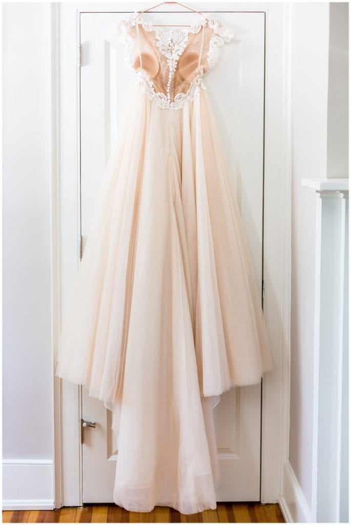 Blush tulle and lace wedding gown hanging in doorway