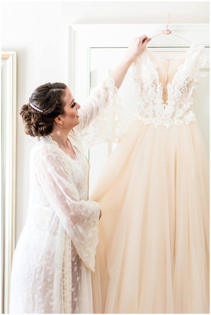 Bride in lace robe reaching for cream lace and tulle wedding gown