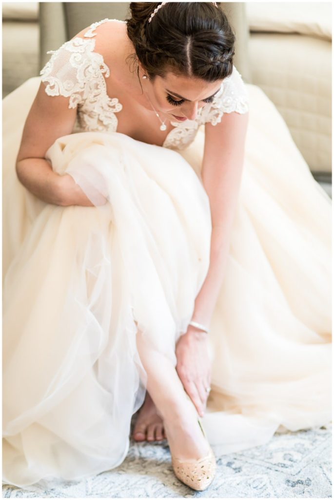 Bride in cream lace and tulle gown putting on tan bridal flats