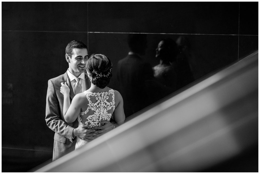 Black and white bride and groom smiling at each other portrait with reflection in stairwell