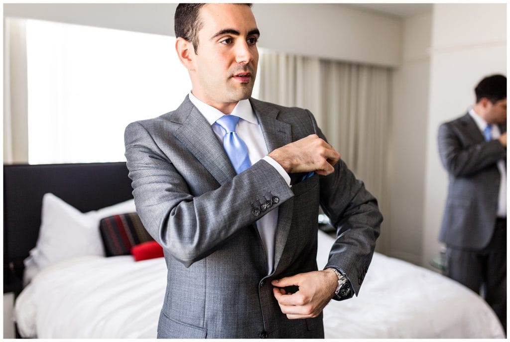 Window lit portrait of groom fixing pocket square at Loews Philadelphia wedding