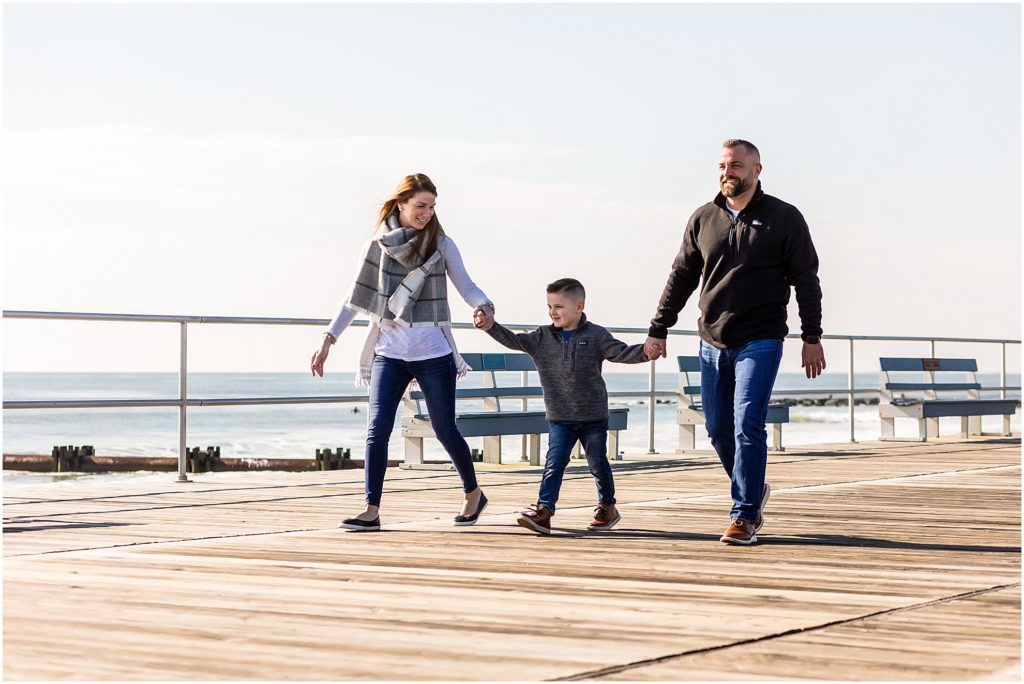 Couple holding hands with child walking down Ocean City New Jersey Boardwalk engagement session