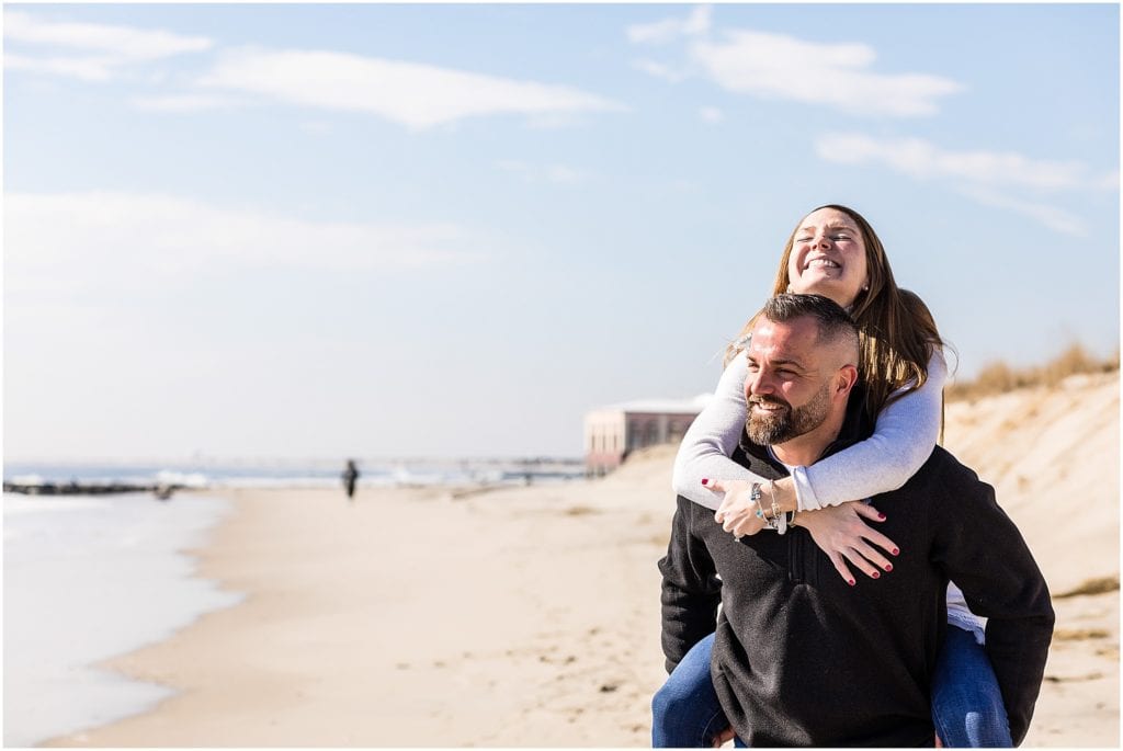 Groom giving bride piggyback ride on Ocean City New Jersey beach engagement portrait