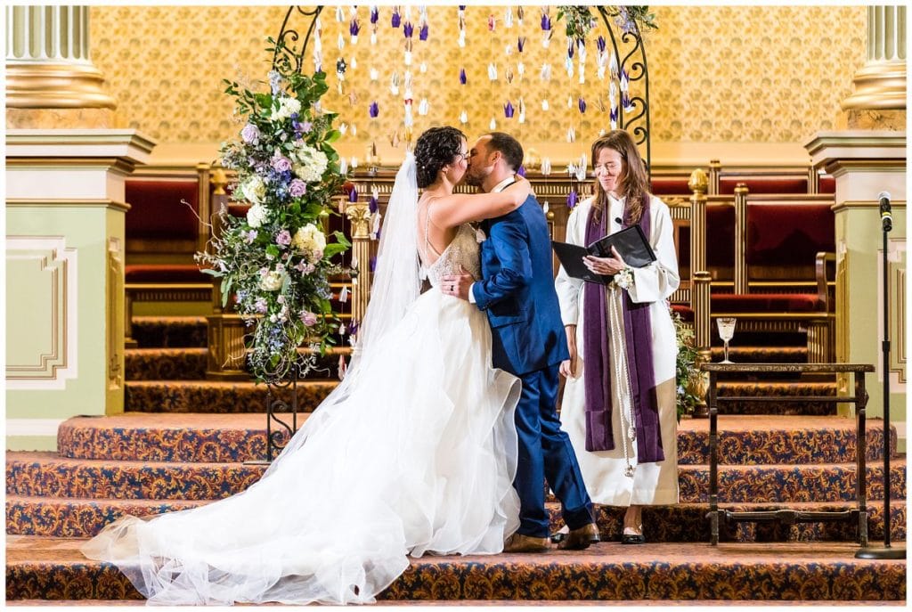 Bride and groom kiss under paper crane archway at One North Broad wedding ceremony