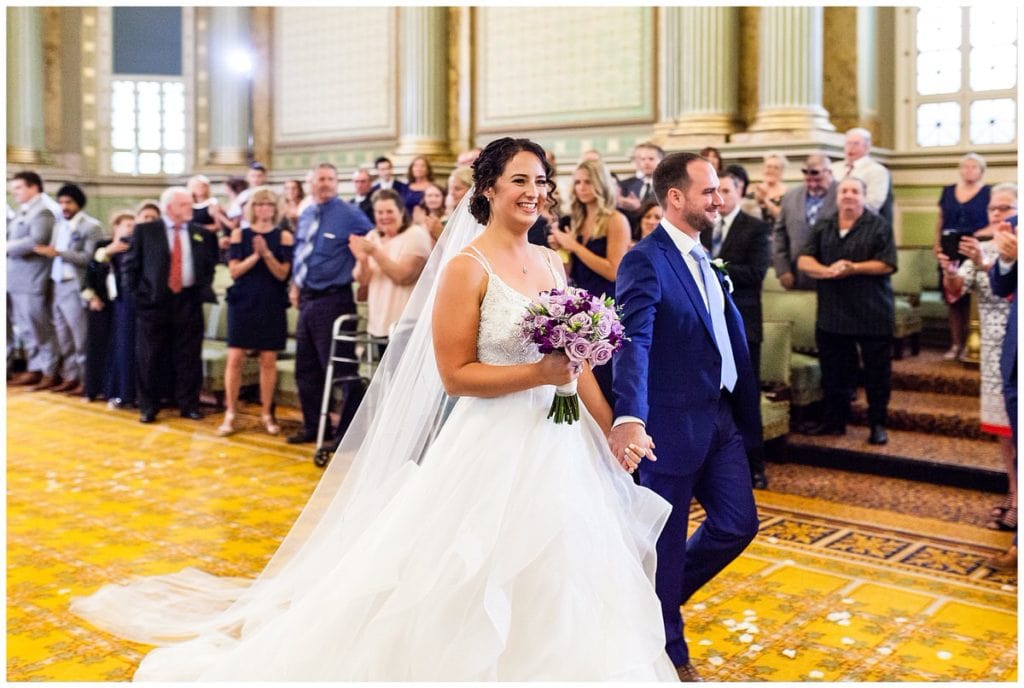 Bride and groom walk up aisle holding hands after wedding ceremony at One North Broad