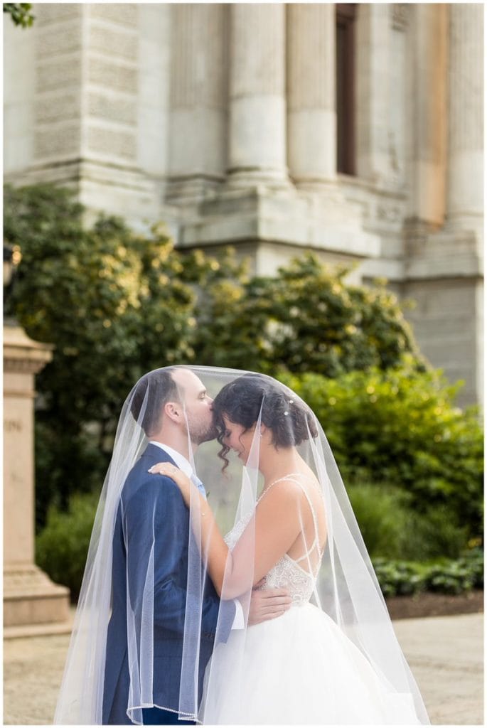 Groom kissing bride on forehead under veil at Philadelphia City Hall