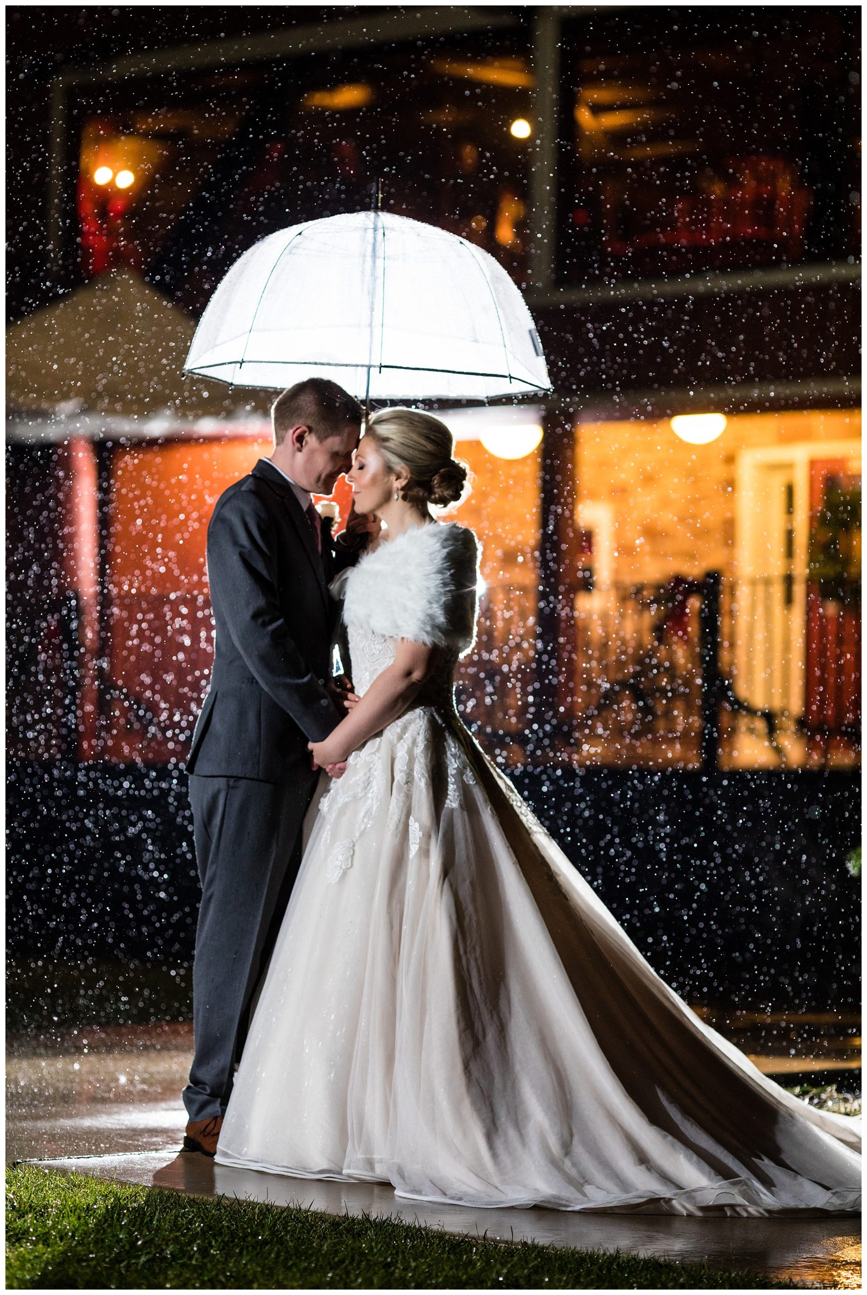Bride and groom snuggle under umbrella in snow at Barn on Bridge holiday winter wedding
