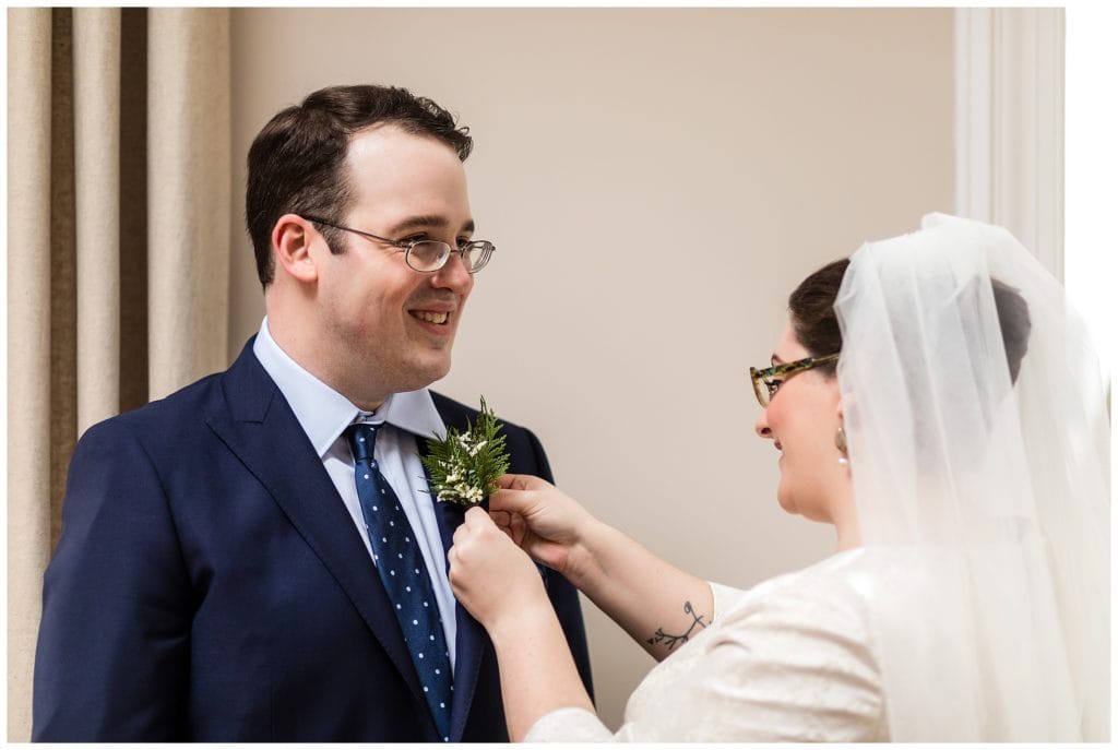 Bride pinning pine boutonniere on groom before intimate wedding ceremony at Malvern Buttery