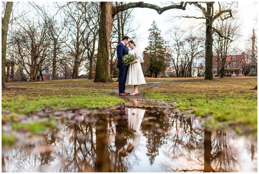 Romantic bride and groom portrait in tree filled yard with reflection in puddle