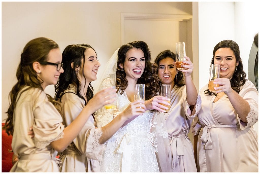 Bride and bridesmaids in matching blush robes toasting champagne while getting ready at the Loews Philadelphia