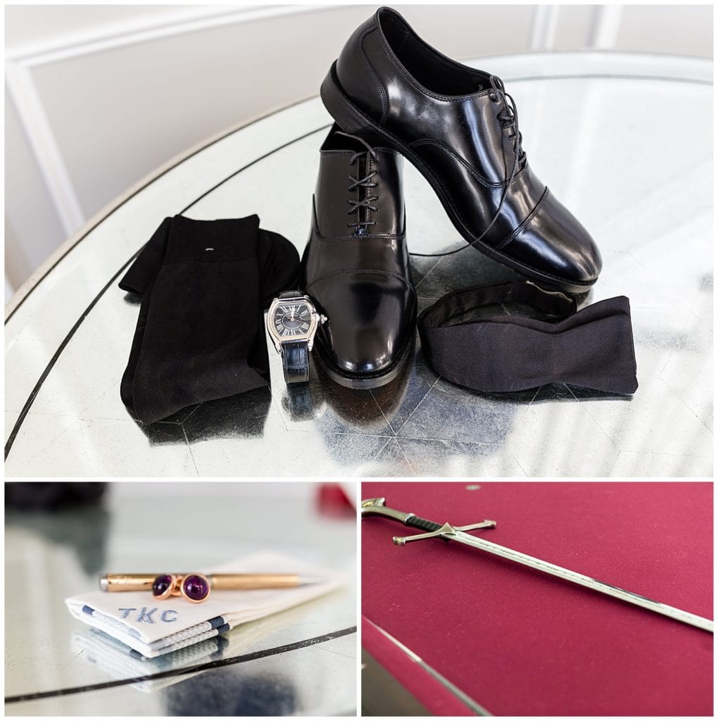 Groom wedding accessories collage with black dress shoes, tie, and watch, monogrammed handkerchief, gold and red stone cufflinks, and sword on pool table