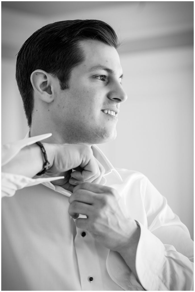 Black and white portrait of groom buttoning dress shirt