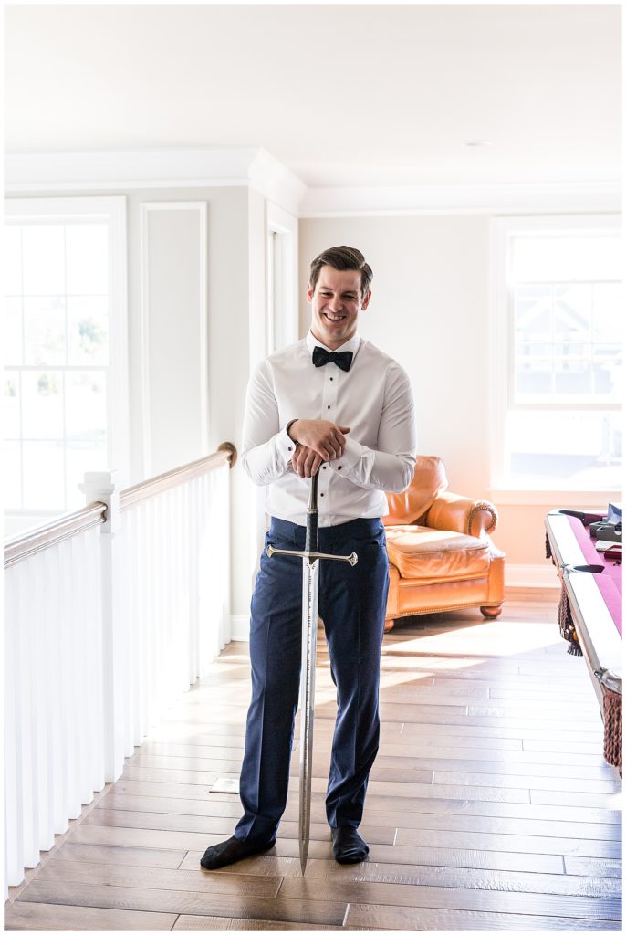 Groom holding sword while getting ready for wedding window lit portrait