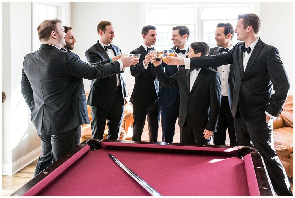 Groomsmen toast with groom over pool table before wedding