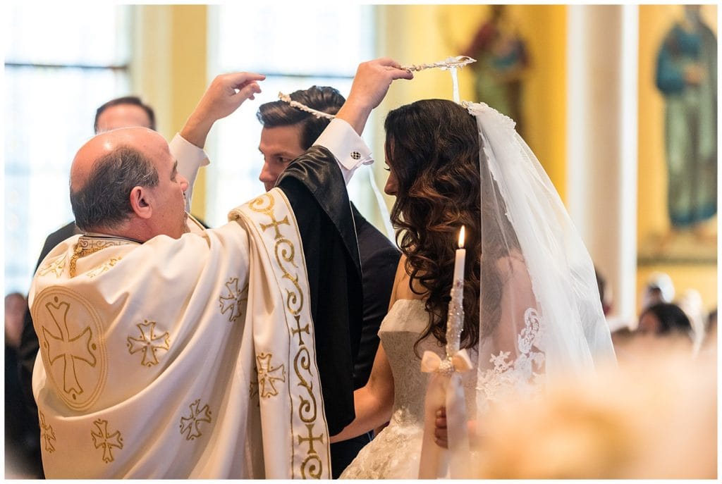 Father placing unity crowns on bride and grooms heads in traditional church wedding ceremony