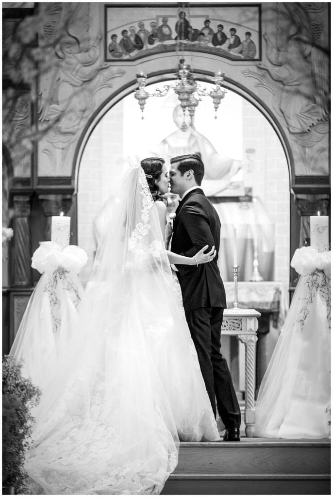Black and white portrait of bride and groom kissing at alter in traditional church wedding