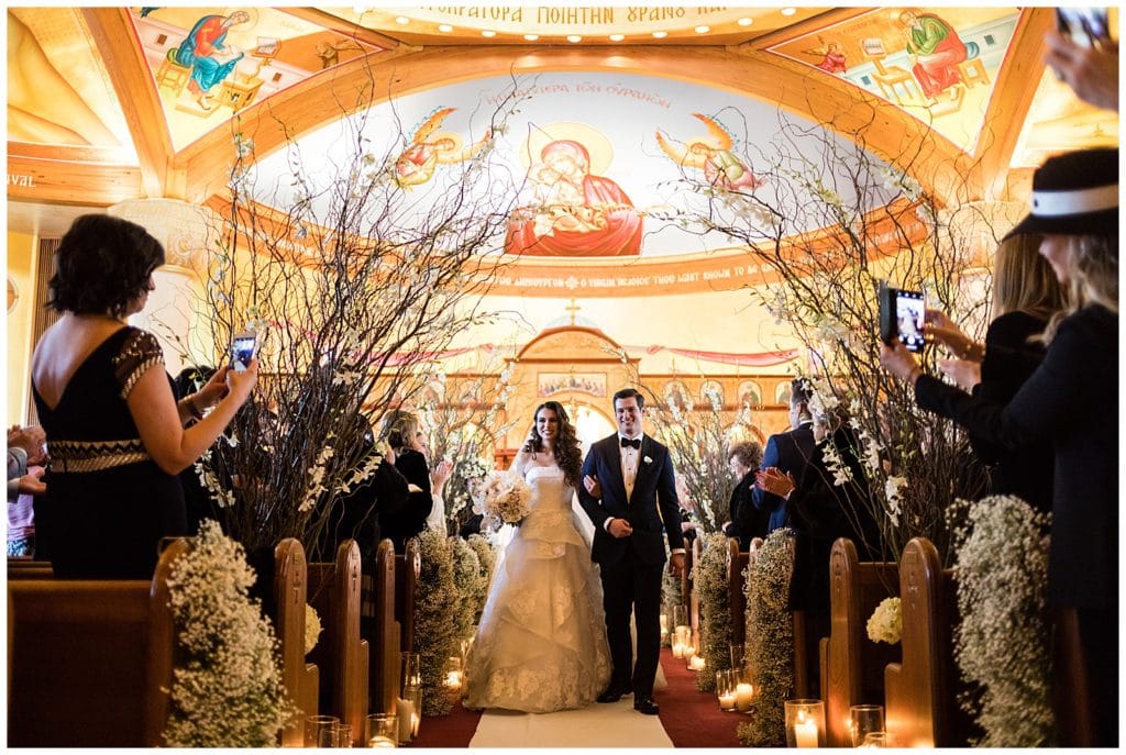 Guests take pictures of bride and groom walking up aisle after traditional church wedding ceremony