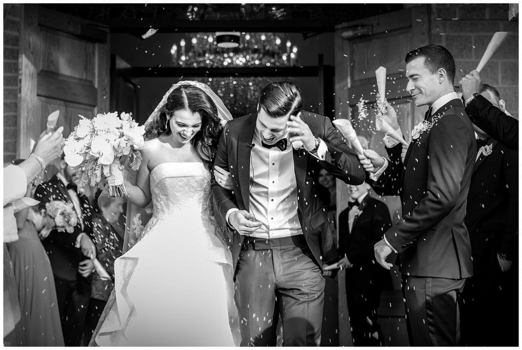 black and white portrait of bride and groom exiting church with guests throwing seeds after traditional church wedding ceremony