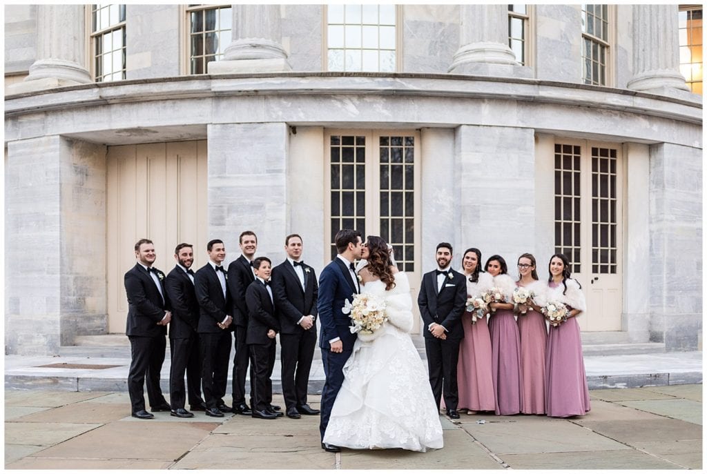 Bride and groom kiss in front of bridesmaids and groomsmen and Merchant Exchange Building