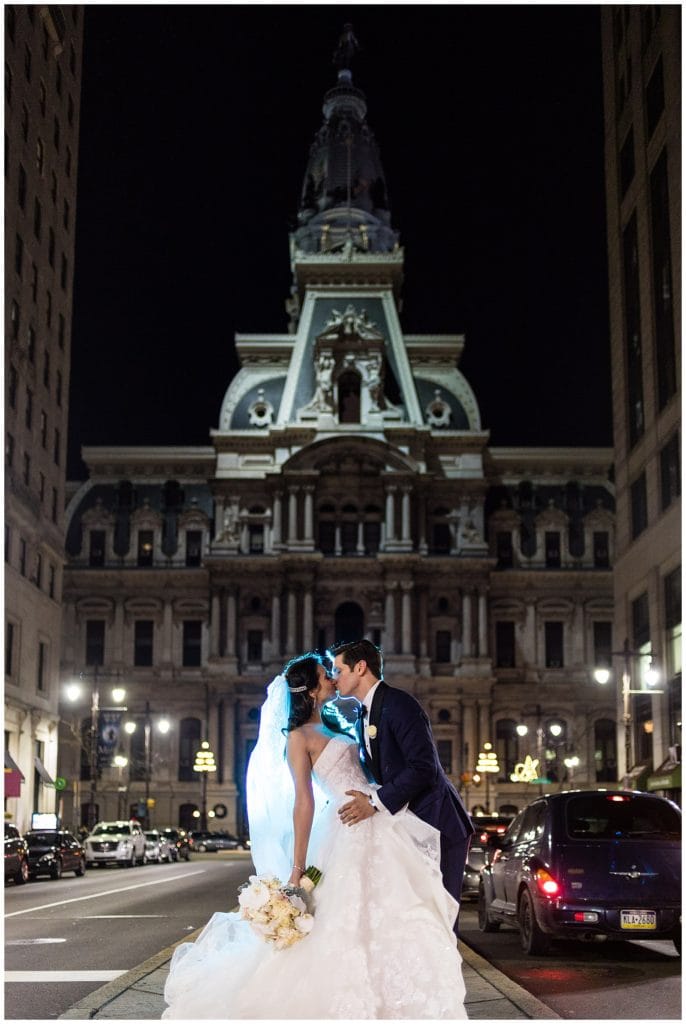 Blue back-lit night shot of bride and groom kissing on Broad Street in front of Philadelphia City Hall