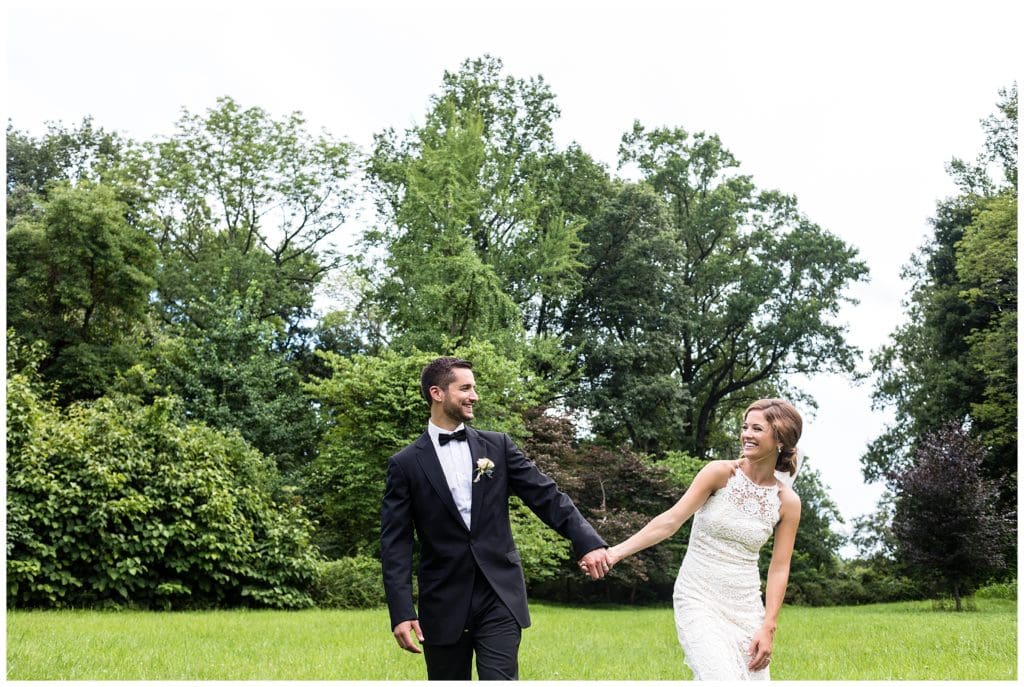 Bride and groom hold hands and walk through field at the Olde Mill Inn wedding