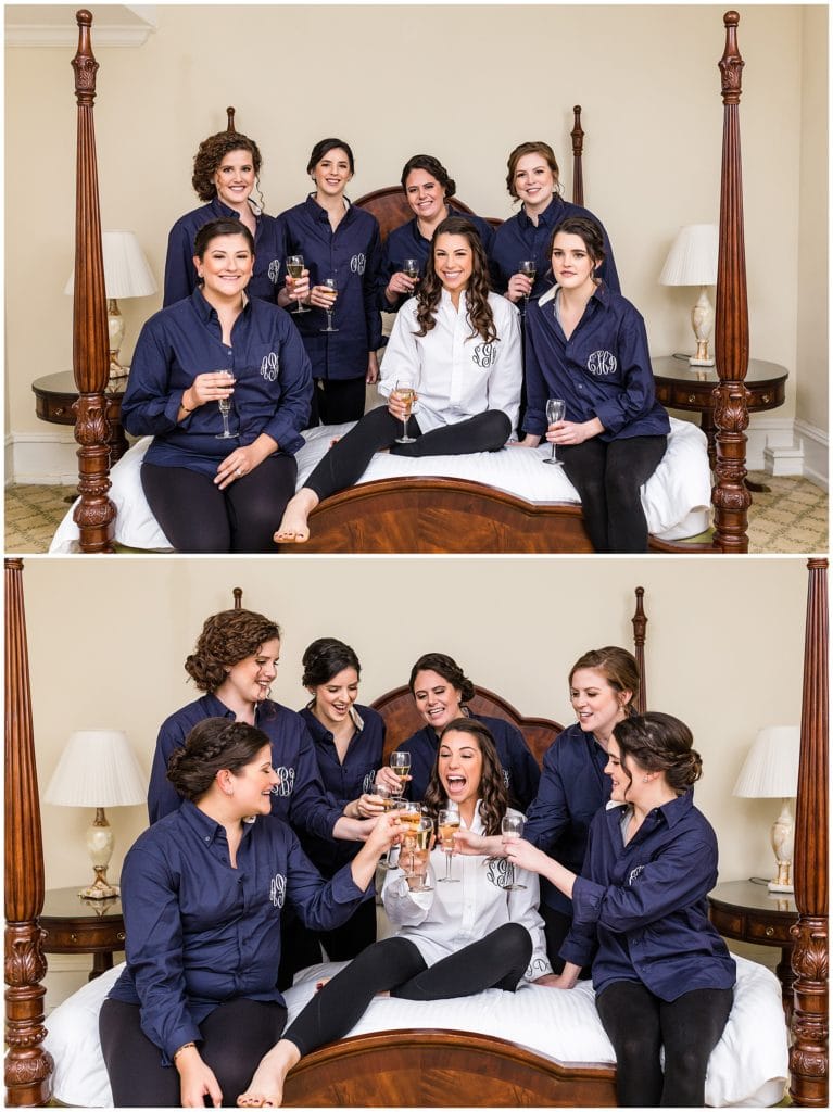 Bridesmaids in matching navy blue button downs with monograms toasting champagne on bed