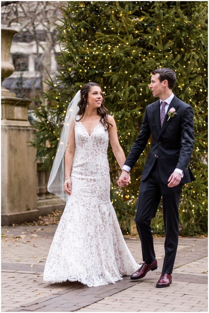 Bride and groom hold hands and walk through Rittenhouse Square Park during winter holiday wedding