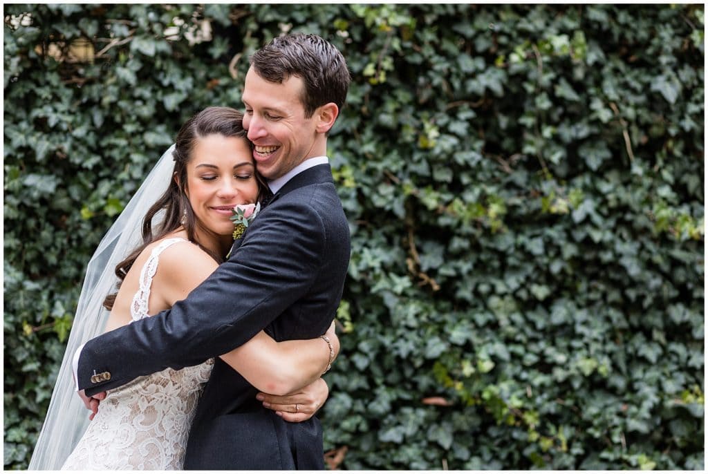 Bride and groom hug in front of ivy wall at Rittenhouse Square Park