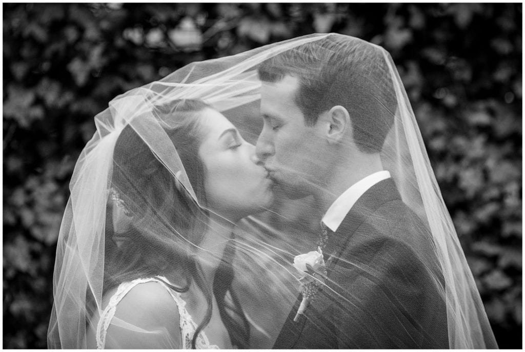 Black and white wedding portrait of bride and groom kissing under veil in Rittenhouse Square Park winter holiday wedding